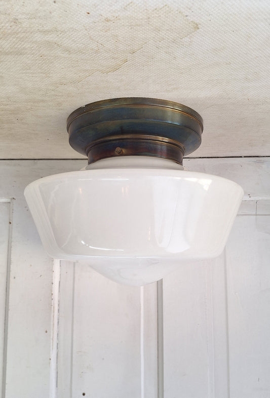 Decorative wall light fixture with white glass shade and brass finish on a textured wall.