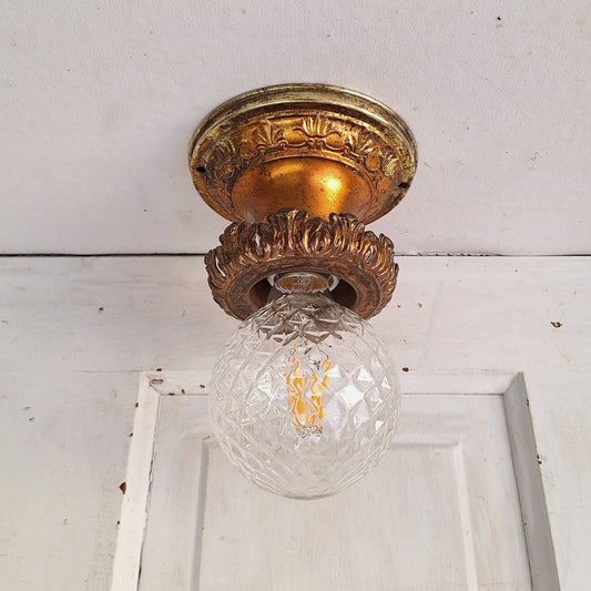 Decorative glass light fixture with gold metal fitting on a white wall.